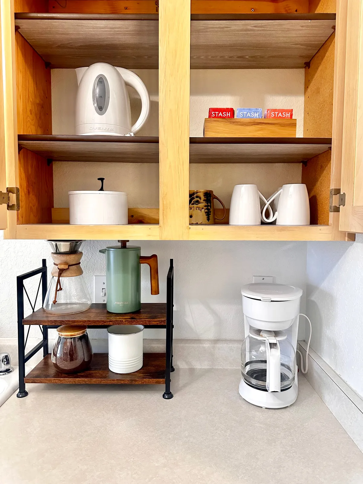 A cozy kitchen corner featuring a white kettle, coffee maker, tea stash boxes, glass coffee maker, and ceramic mugs. The setup suggests the comfort of a hot beverage, making it easy for guests to unwind or prepare for a busy day.