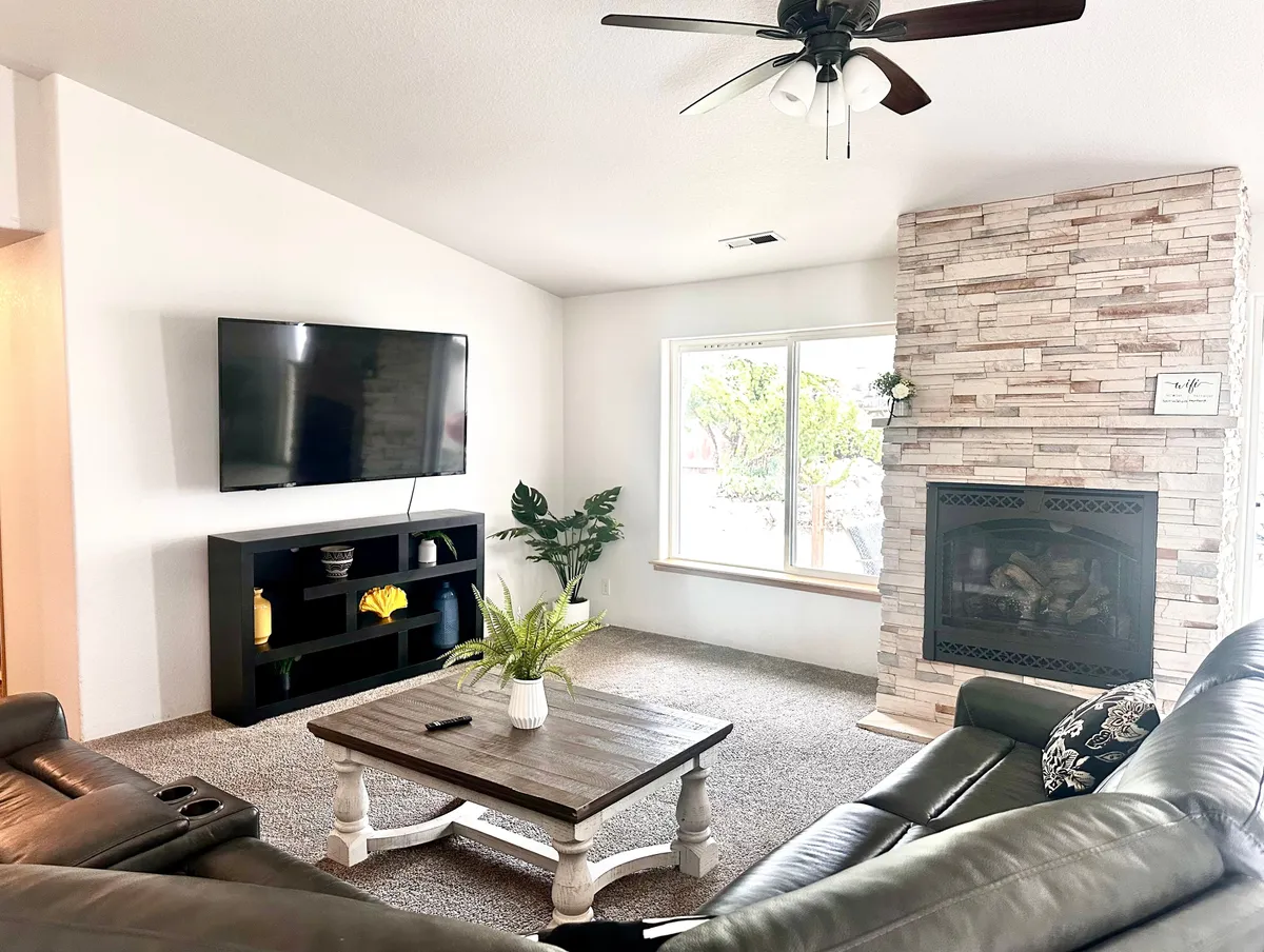 This image features a cozy living room setup with a television, fireplace, inviting sofa, and ample natural light from large windows. The space exudes warmth and is clearly suited for gatherings, movie nights, and intimate conversations, with plush seating and stylish decor.