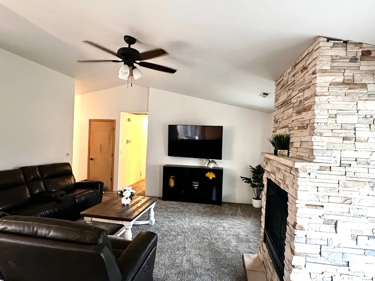 A welcoming family room showcasing a stone fireplace, leather sofas, a large TV, and a central coffee table. The setup is ideal for relaxing, entertaining, or planning group activities, and the warm lighting enhances the inviting mood.