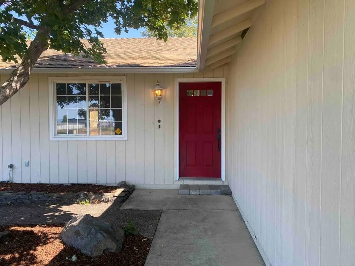 This exterior image captures the home's inviting red front door, large window, and a stone pathway leading to the entrance. The scene suggests a welcoming atmosphere and hints at the property's curb appeal and accessibility.