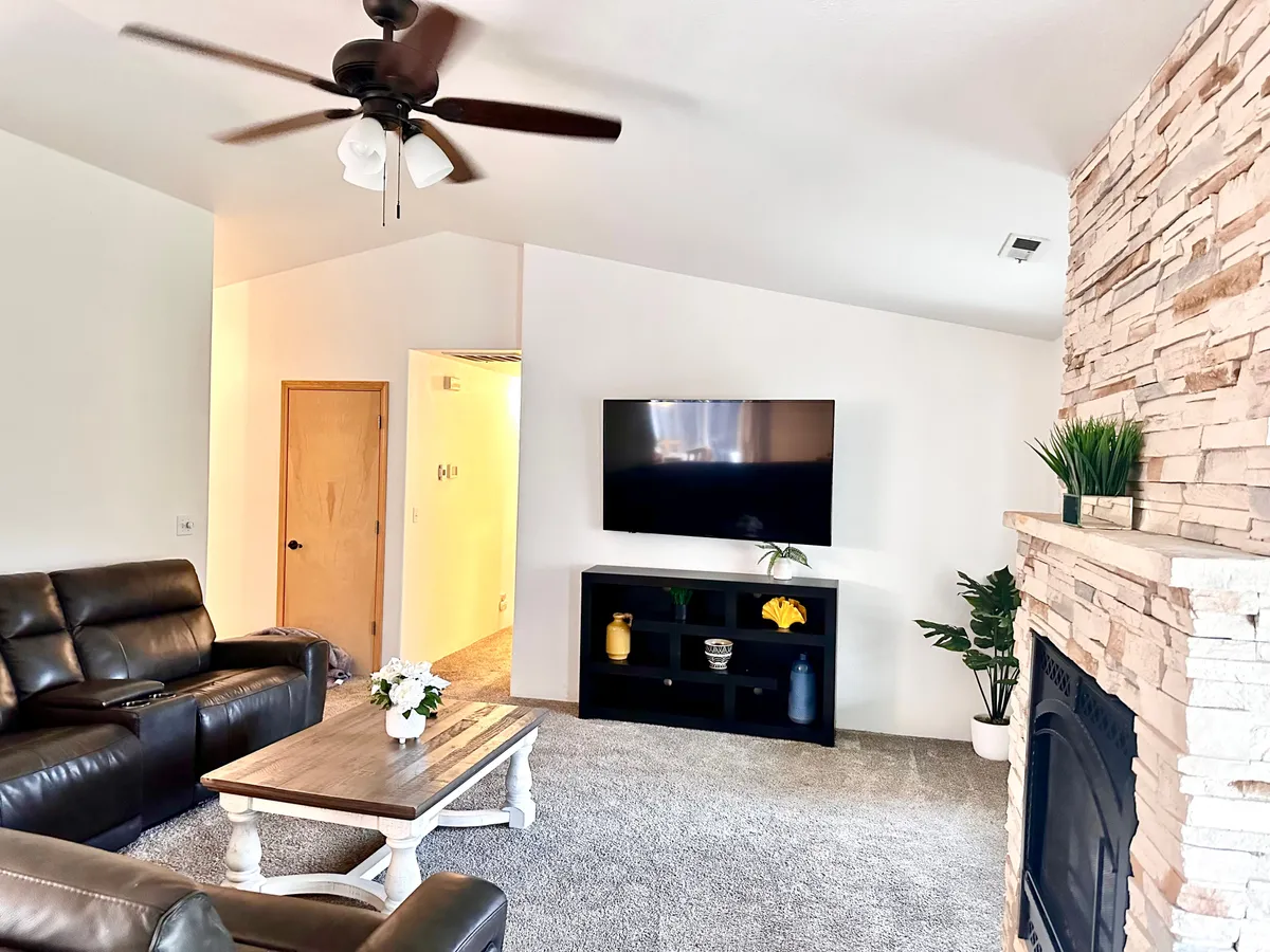 The image showcases a cozy, inviting living room with a plush leather sofa, a stylish coffee table, a warm fireplace, a large TV, and a touch of greenery with a plant on the shelf. The space is designed for relaxing, entertaining guests, or unwinding with a movie or good book.