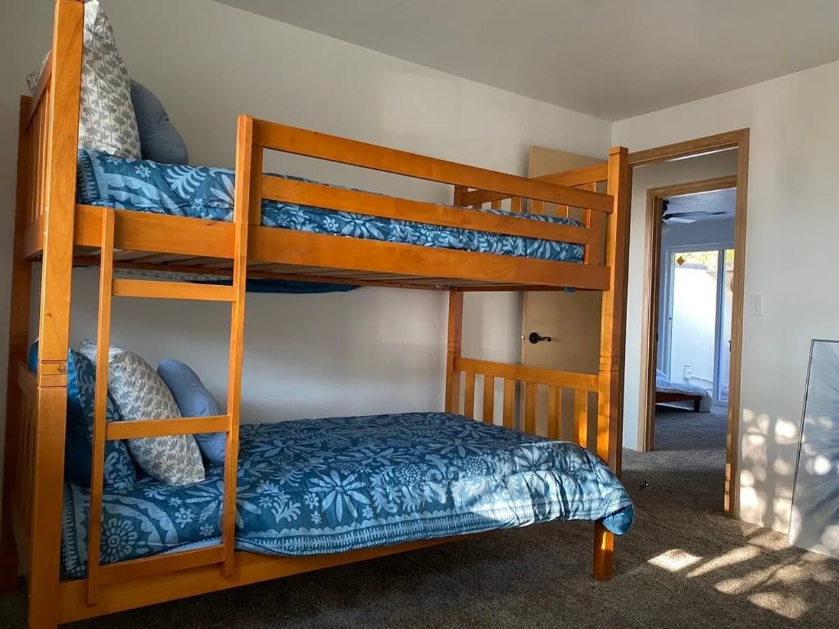 A playful and cozy third bedroom with twin bunk beds dressed in blue patterned bedding and decorative pillows. The setting feels ideal for children or friends, with a focus on comfort and fun.